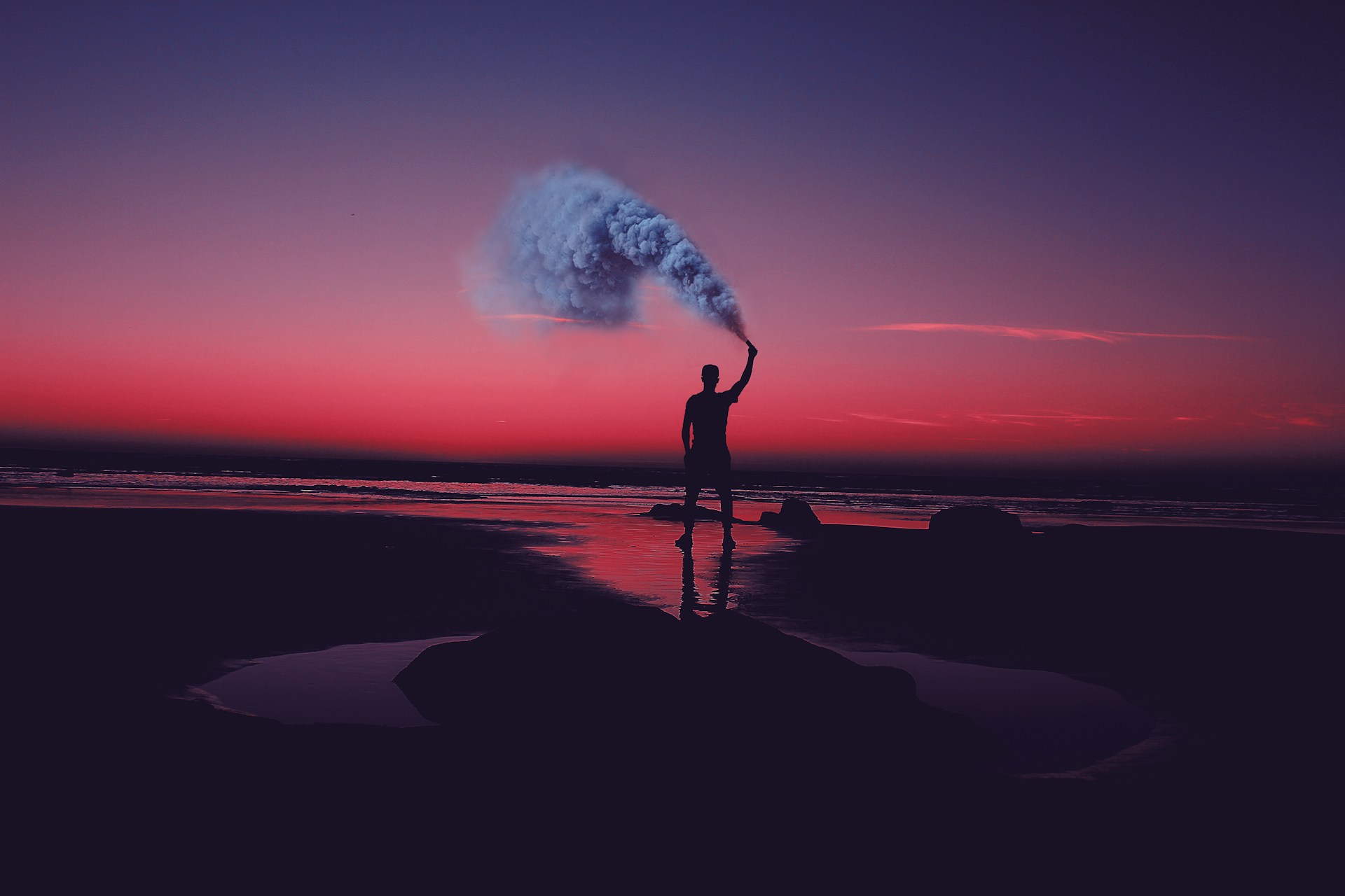 silhouette of man standing on seashore holding smoke can