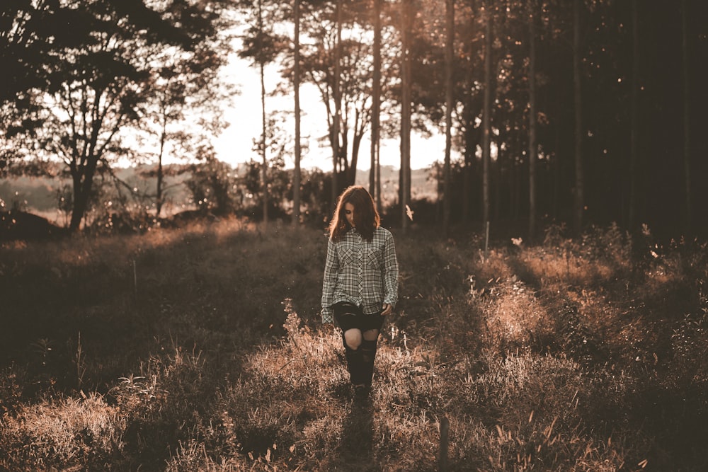 woman walking on brown grass field near trees