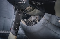 An up-close view of the mechanical parts of an aircraft engine. The image highlights the engine compartment, showcasing various metal components, parts, and textures. The worn and weathered surfaces suggest age and use.