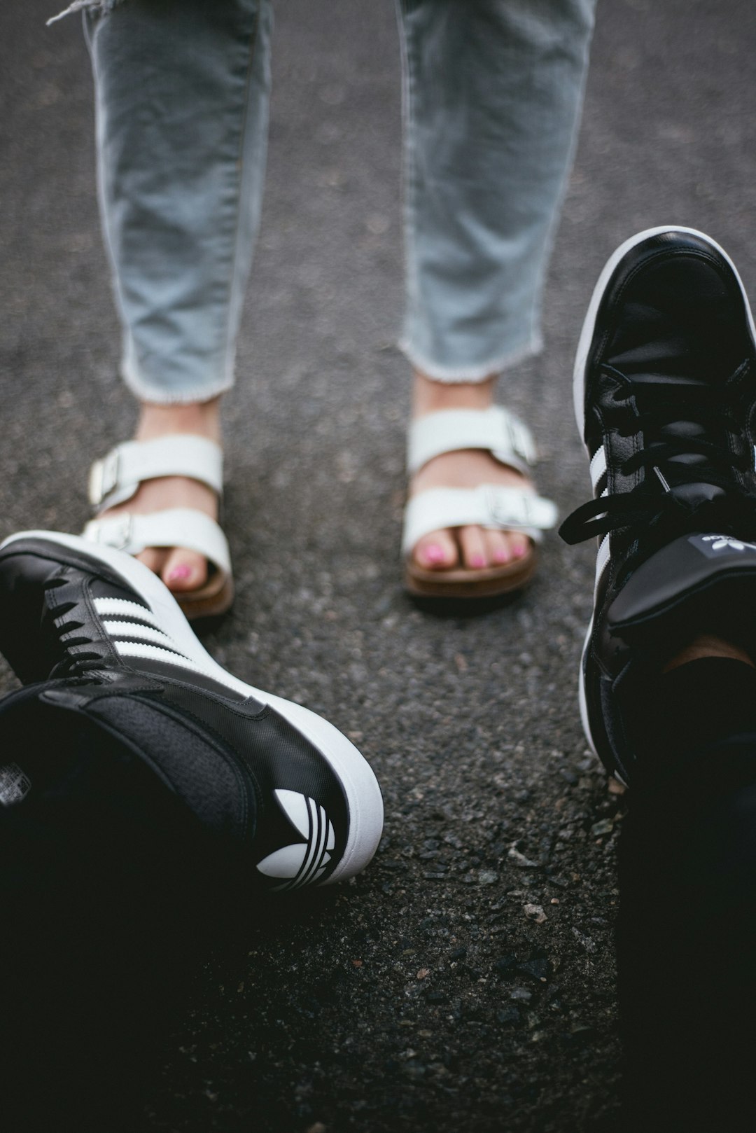 pair of black adiads shoes across person wearing white-and-brown flatbed sandals