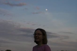 Smiling child wearing bright blue round glasses outdoors.