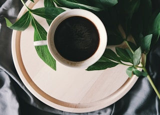 white ceramic mug beside green leaves