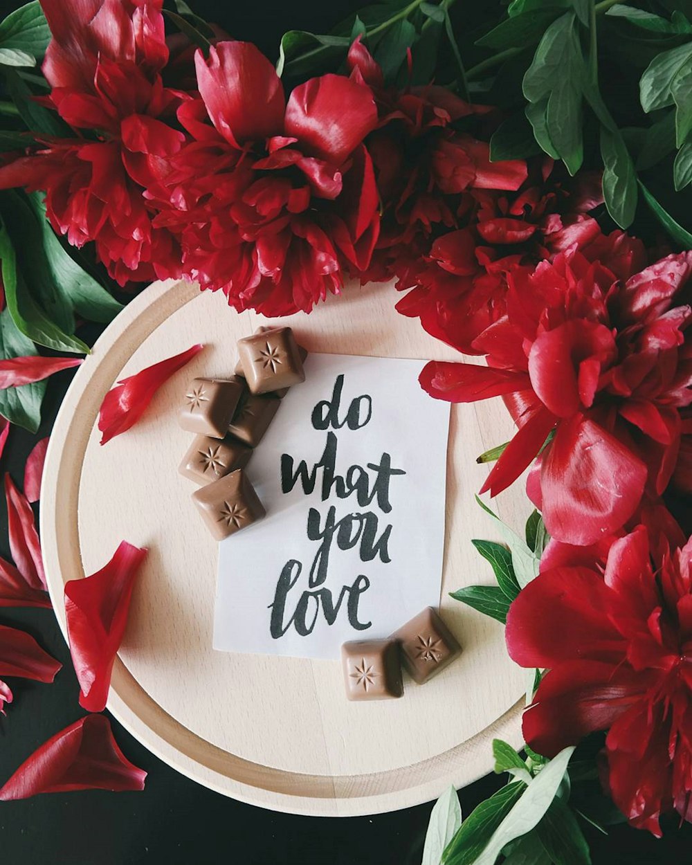Una nota en un pedazo de papel encima de un plato junto a flores rojas que dice "Haz lo que amas".
