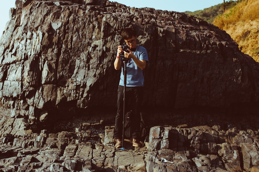 man holding camera while standing on cliff during daytime