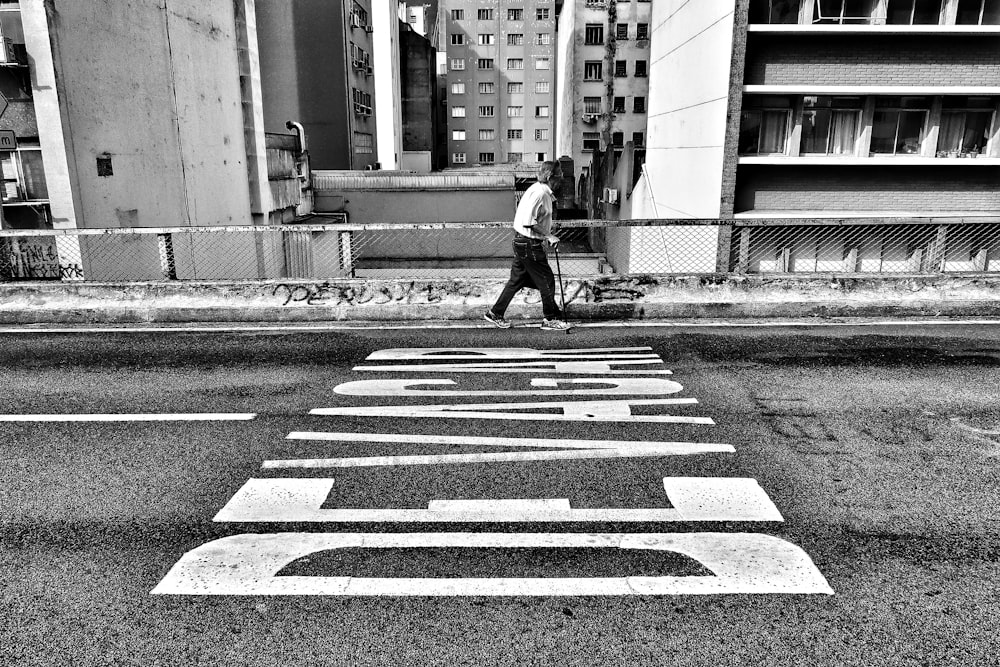 Fotografía en escala de grises de una persona caminando al lado de la carretera pavimentada