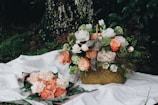 A delicate bridal bouquet featuring soft peach roses, white ranunculus, and lush greenery arranged organically on a rustic wooden table.