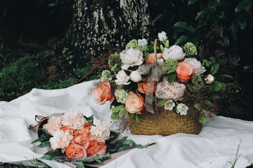 A delicate bridal bouquet featuring soft peach roses, white ranunculus, and lush greenery arranged organically on a rustic wooden table.