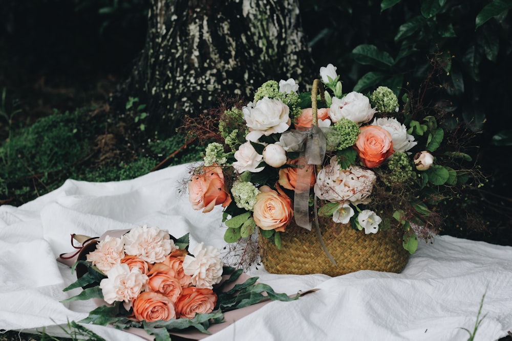 Roses and peonies in a basket and a bouquet on white cloth on the ground