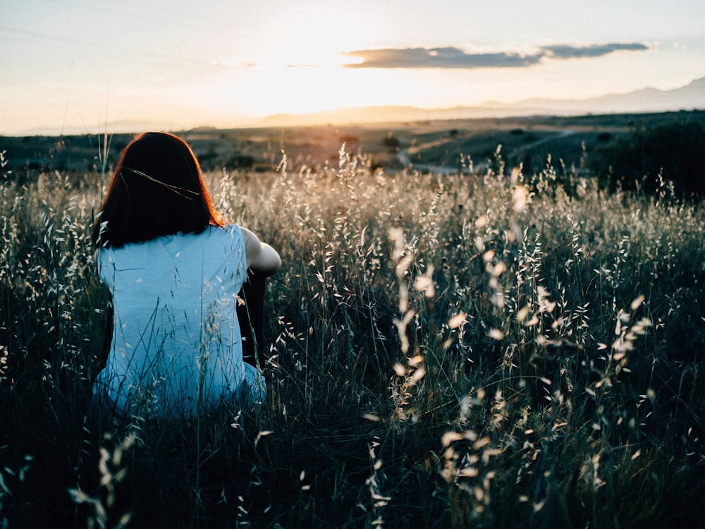 Mujer sentada en el campo de hierba viendo la puesta del sol