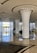 A modern and spacious hotel lobby featuring two large intricately designed columns with a leaf-like pattern. The area is bright and airy, with a high ceiling and shiny, reflective marble floors. Large floor-to-ceiling windows allow natural light to flood the space, and there is a reception desk in the background. Potted plants add a touch of greenery.