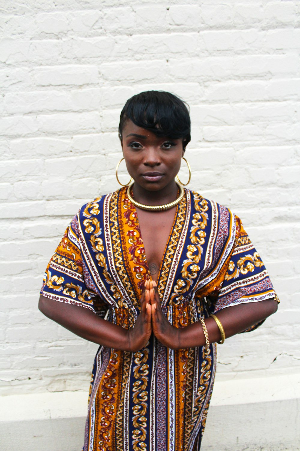 Uma mulher afro-americana usando brincos de argola, colocando as mãos juntas em uma oração.