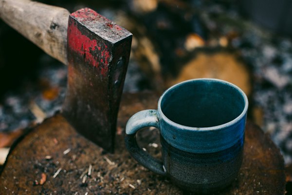 An enamel cup and an axe at a campfire — Yellowknife, Canada