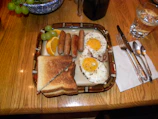 A hearty breakfast plate with eggs, sausage, toast, and fresh fruit on a wooden table.