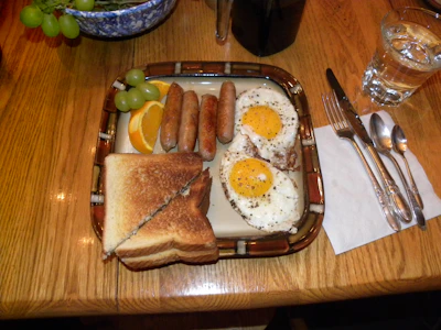 A hearty breakfast plate with eggs, sausage, toast, and fresh fruit on a wooden table.