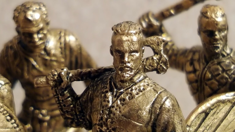 Bronze figurines of warriors are depicted, featuring detailed armor and weapons like axes and swords. The figures appear to be in dynamic poses, suggesting action or readiness for battle.