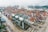Aerial view of a bustling shipping port with numerous cargo containers and large cranes. The scene is filled with containers of various colors organized in rows, indicating a high level of activity. The cranes are strategically positioned to load and unload ships docked at the port.