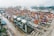 Aerial view of a bustling shipping port with numerous cargo containers and large cranes. The scene is filled with containers of various colors organized in rows, indicating a high level of activity. The cranes are strategically positioned to load and unload ships docked at the port.
