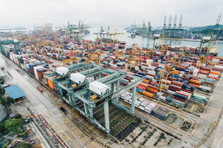 Stacks of multicolored shipping containers under gantry cranes at a port terminal
