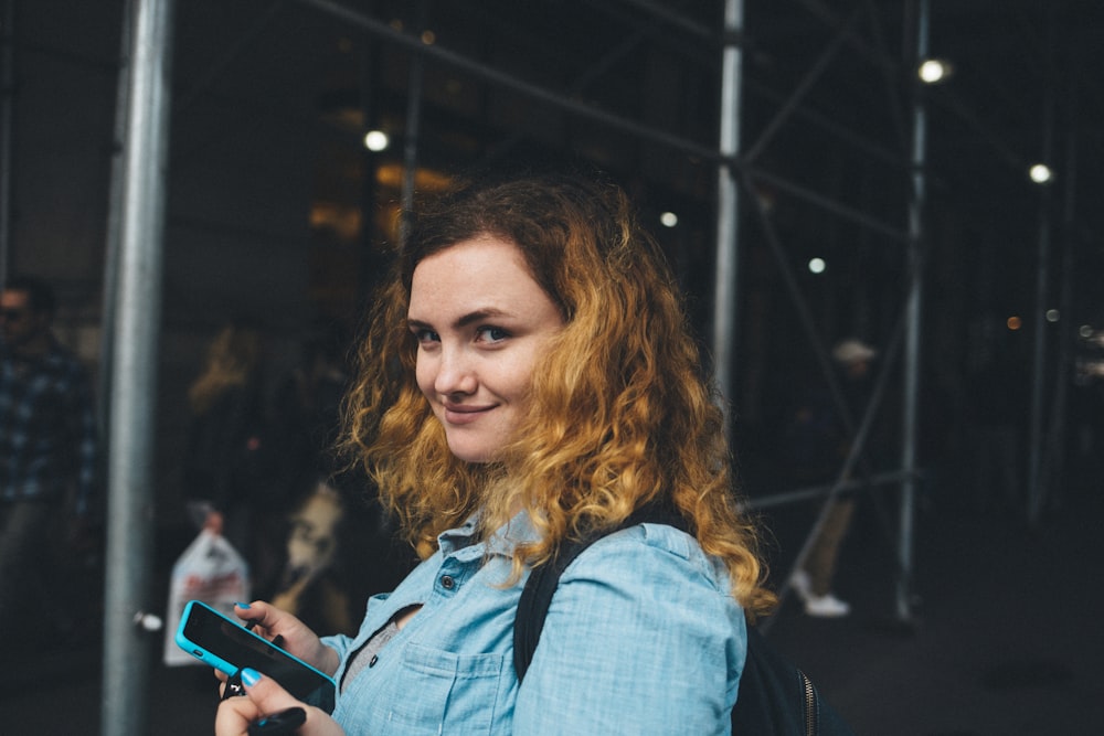 woman holding black smartphone near gray metal frame at daytime