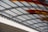Curved metal beams and supporting structures form a canopy with alternating clear and tinted panels. The structure features red and amber hues, adding a vibrant contrast to the metallic tones.