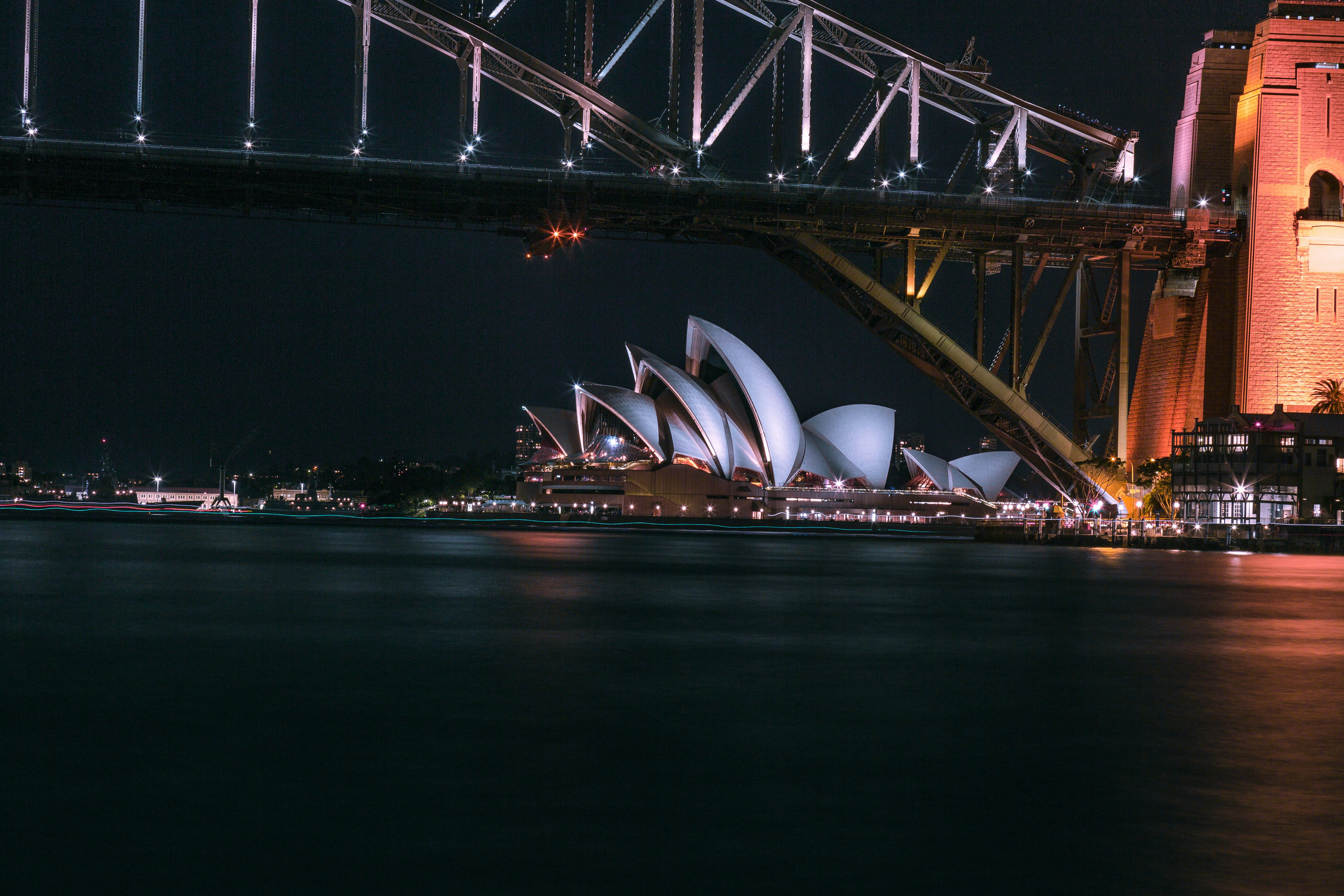 Sydney Opera House at night with dramatic lighting reflecting on the harbor, Sydney Harbour Bridge illuminated in the background