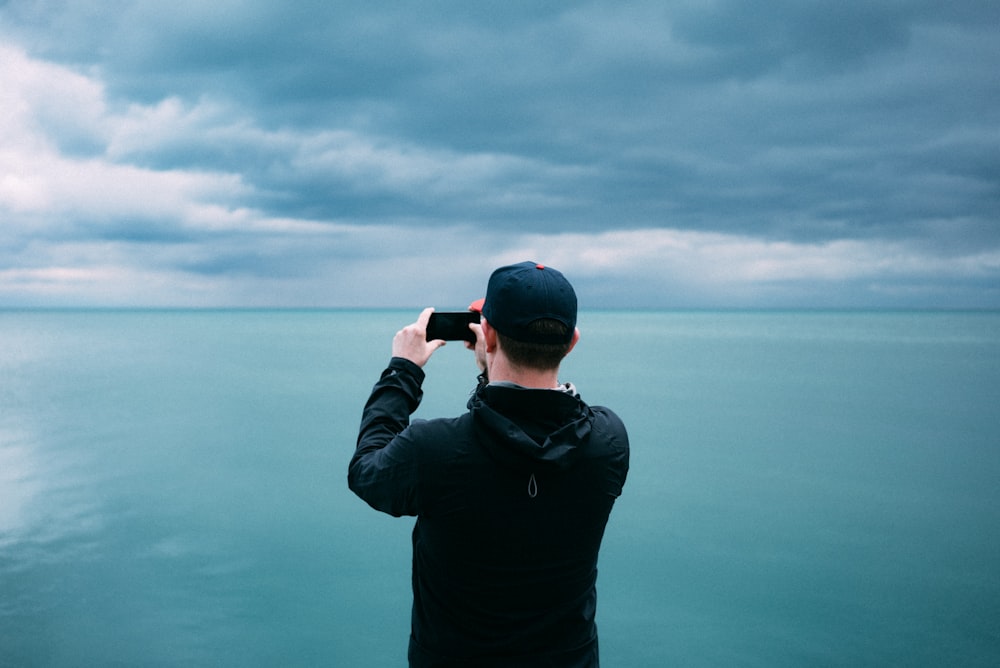 men's black hoodie in front of teal sea