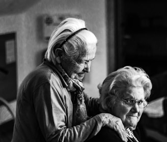 greyscale photo of woman standing behind woman sitting on chair