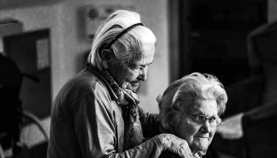 greyscale photo of woman standing behind woman sitting on chair