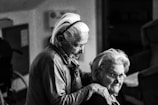 greyscale photo of woman standing behind woman sitting on chair