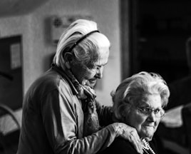 greyscale photo of woman standing behind woman sitting on chair