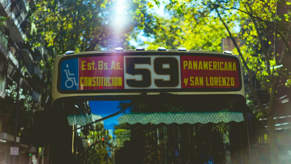 black and red bus showing signage near white high-rise building and green leafed trees during daytime