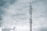 A tall communication tower reaches into a cloudy sky, with several antennas mounted on its structure. The clouds appear thick and grey, suggesting an overcast day.