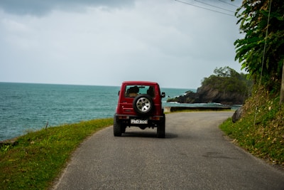 A vibrant SUV driving along a coastal road under a clear blue sky.