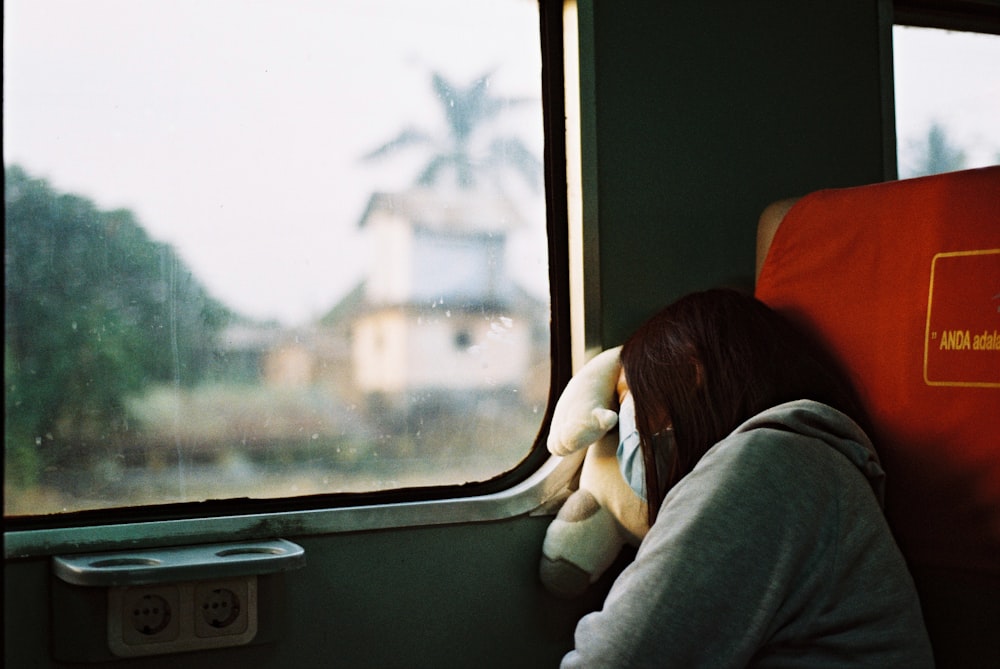 Mujer con sudadera con capucha gris durmiendo en un tren con máscara facial