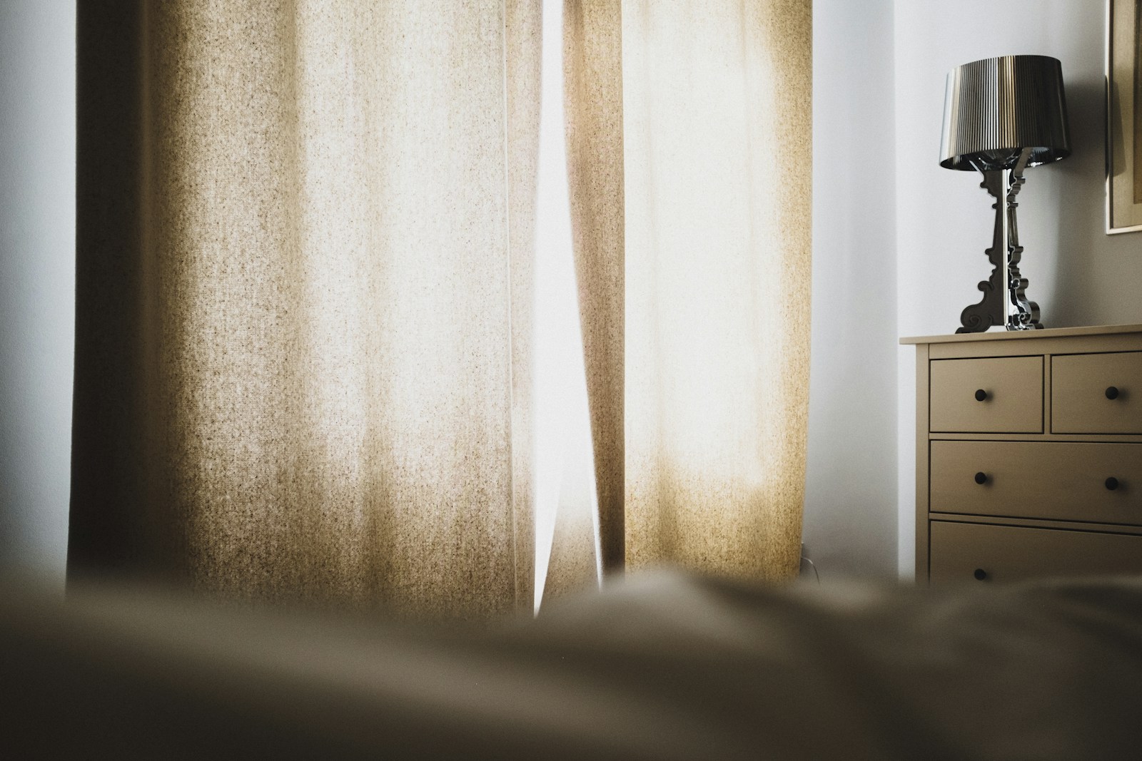 curtain panel and bedside lamp in dim small apartment bedroom