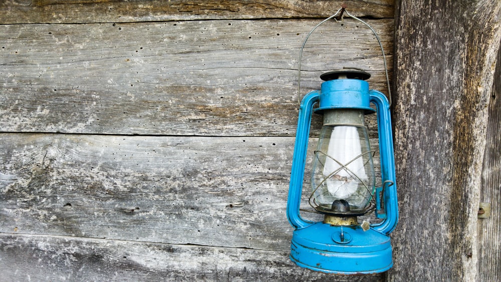 Lámpara de queroseno azul colgada en pared de madera