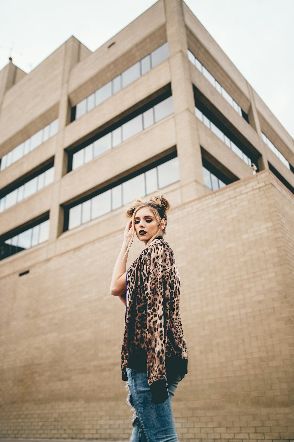 woman with hand on hair standing in front of brown wall