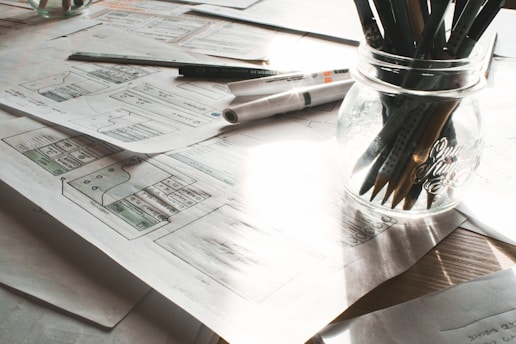 A professional workspace with trading charts, marketing plans, and architectural blueprints spread out.