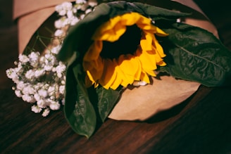Colorful sunflowers standing tall in a rustic wooden basket with green leaves.
