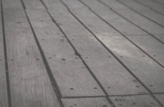 Wooden planks arranged side by side, featuring a slightly weathered texture with visible grains and small holes along the surface.