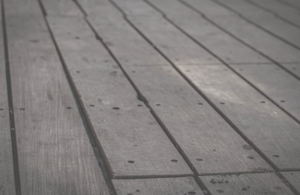 Wooden planks arranged side by side, featuring a slightly weathered texture with visible grains and small holes along the surface.