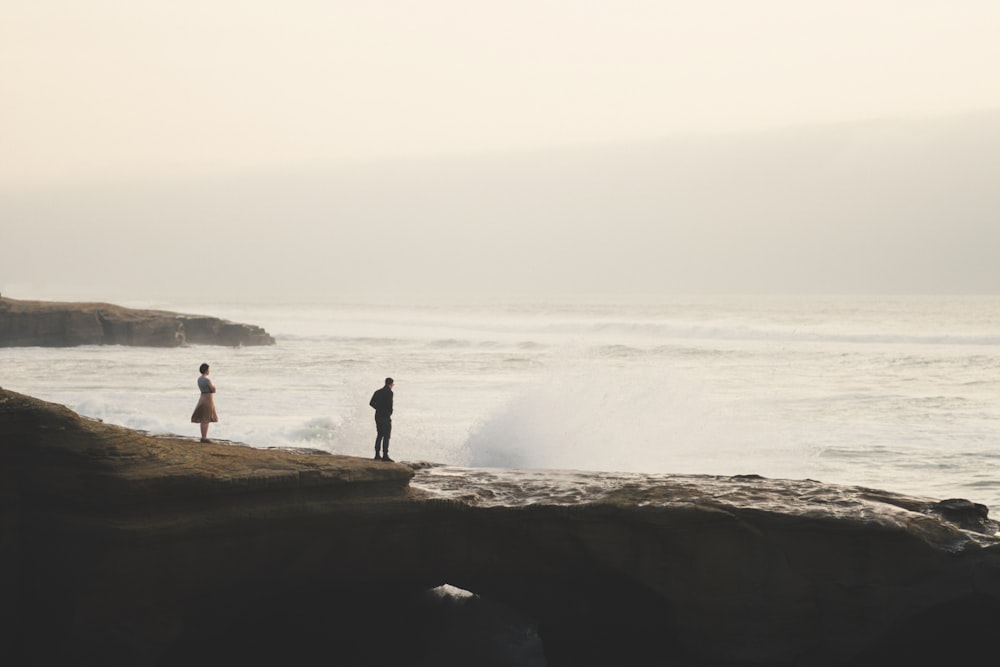 2 person standing on rock near sea during daytime