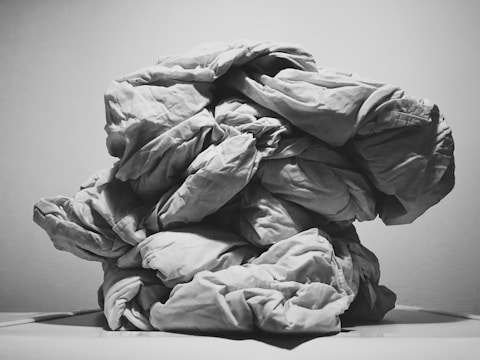 A large, crumpled fabric or sheet piled on a flat surface, creating a textured and abstract shape. The monochrome setting highlights the curves and folds of the material.