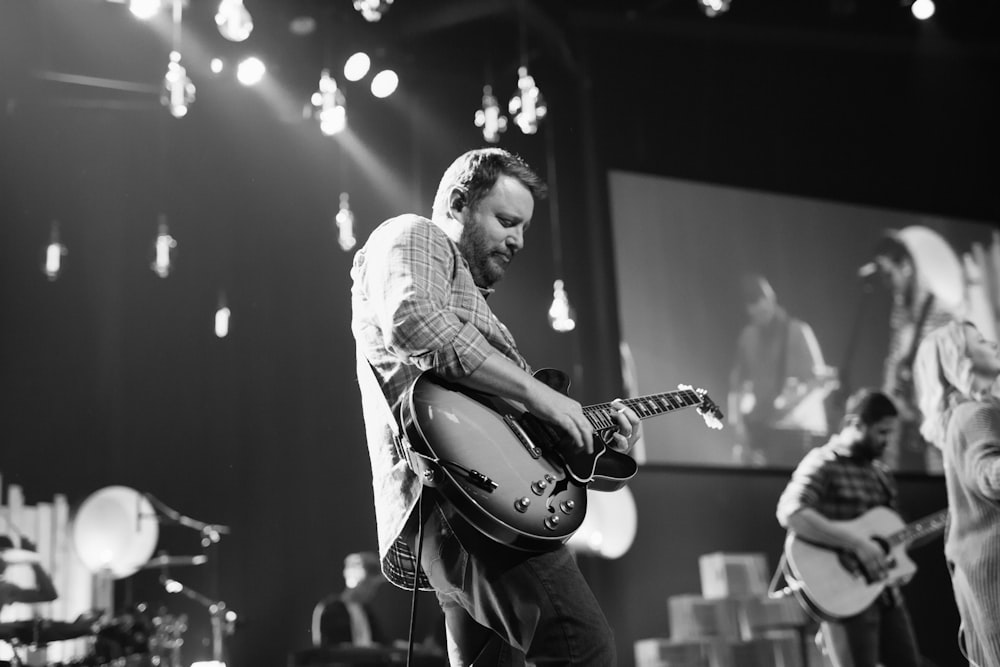 greyscale photo of man playing electric guitar on stage