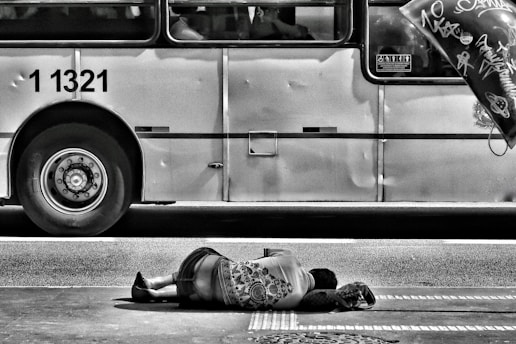 grayscale photography of person laying on ground near bus