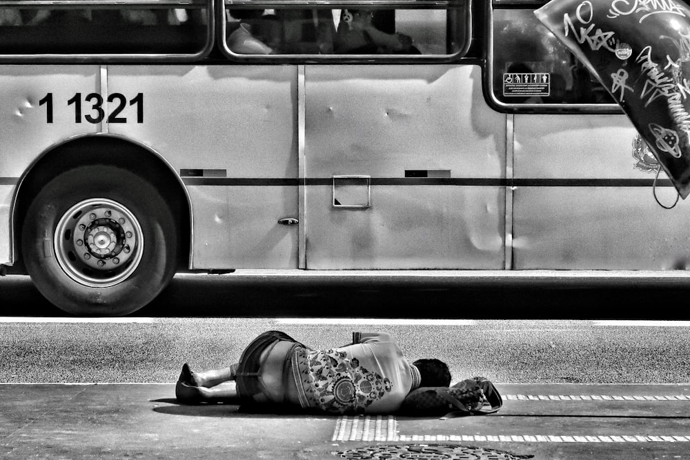 fotografia em tons de cinza da pessoa deitada no chão perto do ônibus