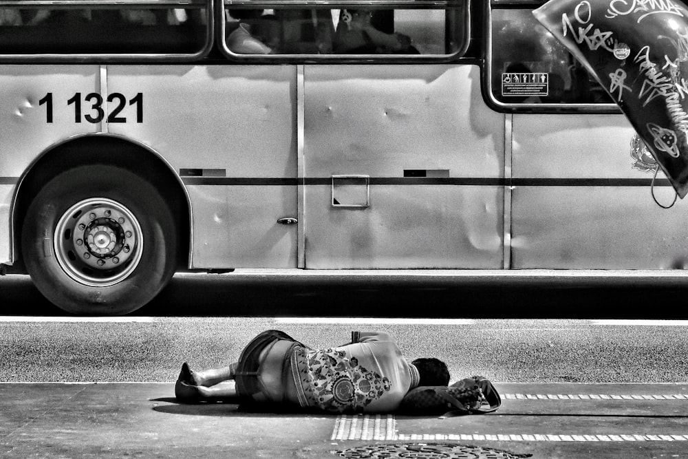 Graustufenfotografie einer Person, die in der Nähe des Busses auf dem Boden liegt