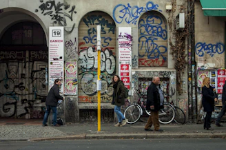 Urban street view capturing graffiti art on a weathered wall with pedestrians passing by.