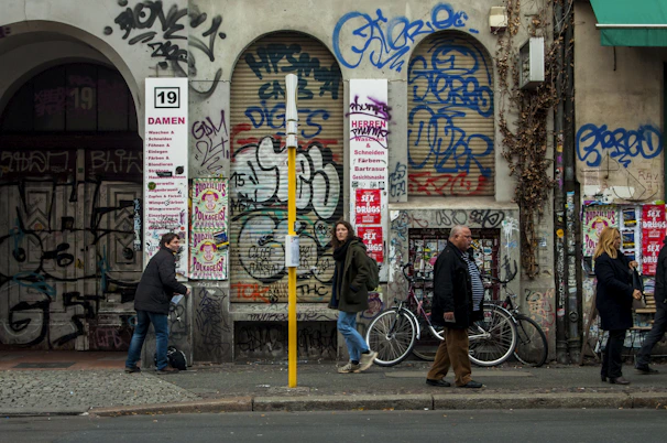 Urban street view capturing graffiti art on a weathered wall with pedestrians passing by.
