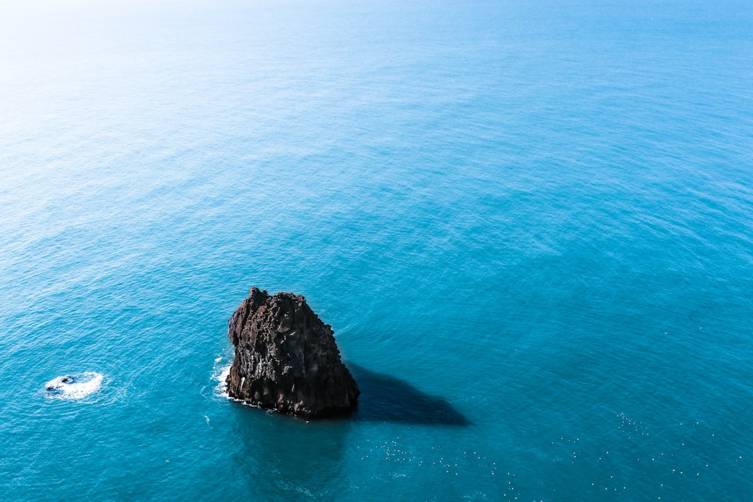 a large black rock in the middle of the bright blue sea